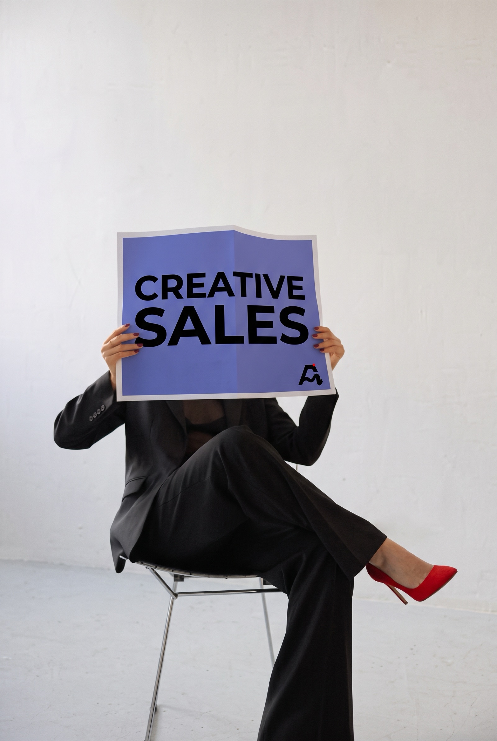 Persona sentada que se cubre el rostro con un cartel de Merkads que dice «Creative Sales»