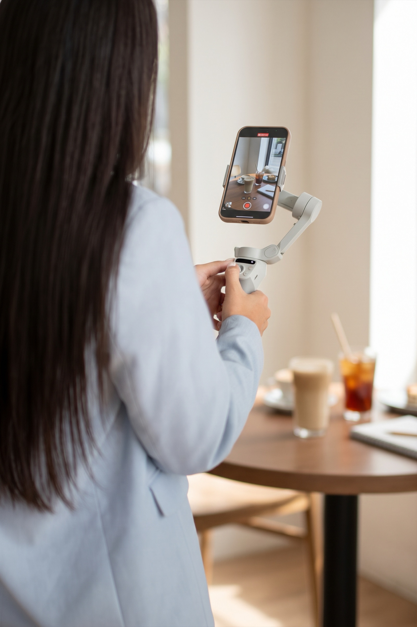 Persona grabando contenido con un celular montado en un estabilizador, en una cafetería con luz natural