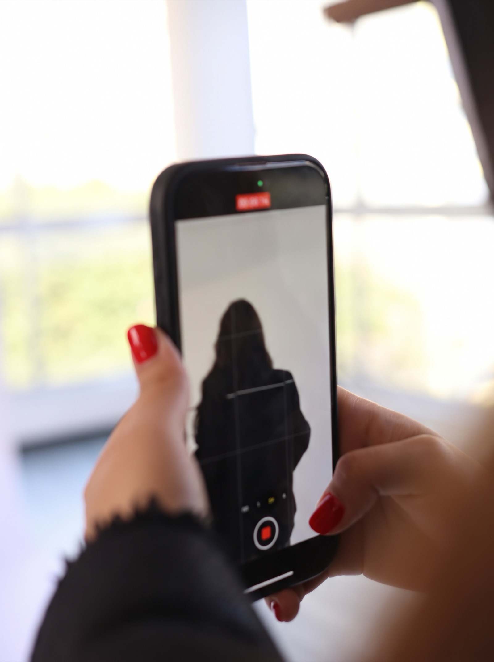 Manos con uñas rojas grabando a una persona con un celular para redes sociales